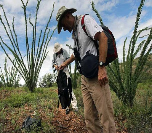 GREEN VALLEY, AZ - JULY 31: Volunteer Tim Doherty inspects (C) a backpack cast away by immigrants crossing from Mexico into Arizona on a backcountry trail as fellow volunteer Rebecca Fowleron watches on July 31, 2010 near Green Valley, Arizona. Doherty conducts patrols for the non-profit Samaritans, delivering water to points near the U.S. Mexico border for immigrants crossing illegally into Arizona. He and fellow volunteers also provide medical assistance for distressed migrants, who often suffer from severe dehydration while crossing the desert. Immigrant aid groups and law enforcement alike say that the number of immigrants crossing illegally into Arizona from Mexico has slowed dramatically in 2010, with jobs scarce due to the U.S. recession and widespread fear in the Latino community associated with Arizona's new immigration enforcement law SB 1070. (Photo by John Moore/Getty Images) *** Local Caption *** Tim Doherty;Rebecca Fowleron
