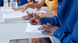 Man writing in book while sitting with friend