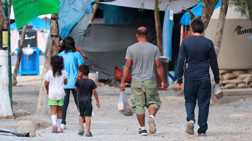 Migrantes caminan entre casas de campaña