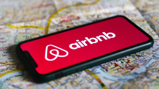 A cellphone has the Airbnb logo pulled up as the phone rests on a map