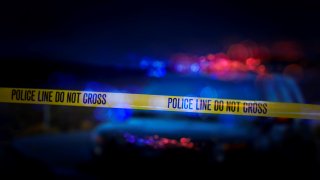 A stock photo of a Police Line "Do Not Cross" caution tape with a defocused police car with sirens flashing red and blue.