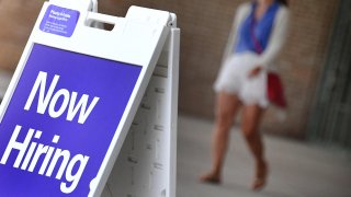 Pedestrians walk by a "Now Hiring" sign