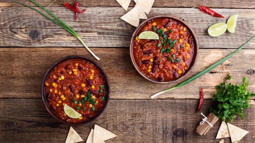 Chili con carne stew served in ceramic bowl on rustic wooden table viewed from above, Mexican cuisine.