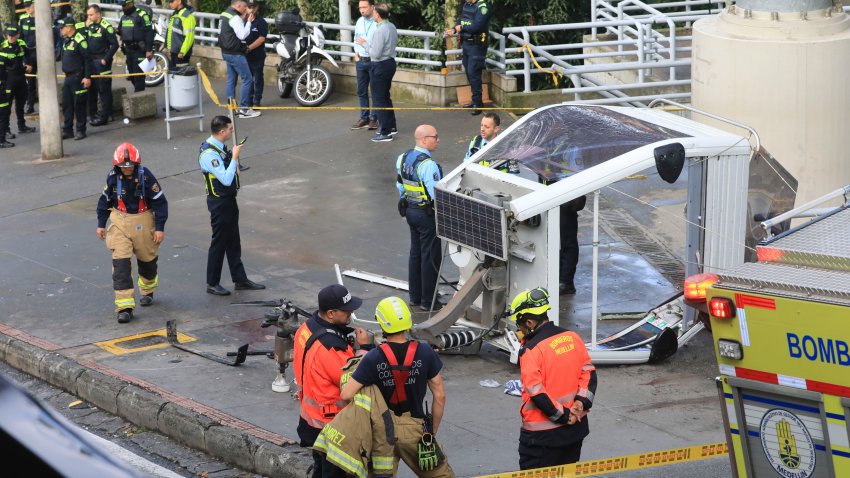 La policía y los bomberos esperan junto a un teleférico tirado en el suelo después de caer en Medellín, Colombia, el miércoles 26 de junio de 2024. Al menos una persona murió y otras 12 resultaron heridas cuando el teleférico se derrumbó mientras se acercaba a una estación, dijeron autoridades locales. (AP Foto/Fredy Amariles)