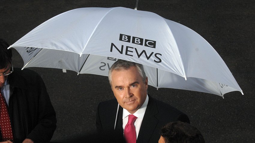 Presenter and newsreader Huw Edwards holds a BBC News umbrella as he reports from outside 10 Downing Street on the day that Gordon Brown took over from Tony Blair as Prime Minister of the UK. Political Correspondent James Landale is just visible left of frame. 27/06/2007. Ten OB OBS outside broadcast broadcasts umbrellas rain London Number (Photo by Jeff Overs/BBC News & Current Affairs via Getty Images)