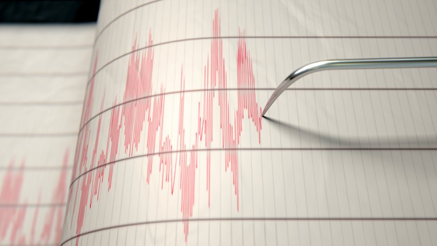 A closeup of a seismograph machine needle drawing a red line on graph paper depicting seismic and earthquake activity