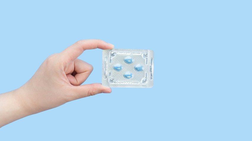 Hands holding sildenafil (Viagra) pills in blister package on blue background. Indication of sildenafil is treatment of erectile dysfunction, pulmonary arterial hypertension.