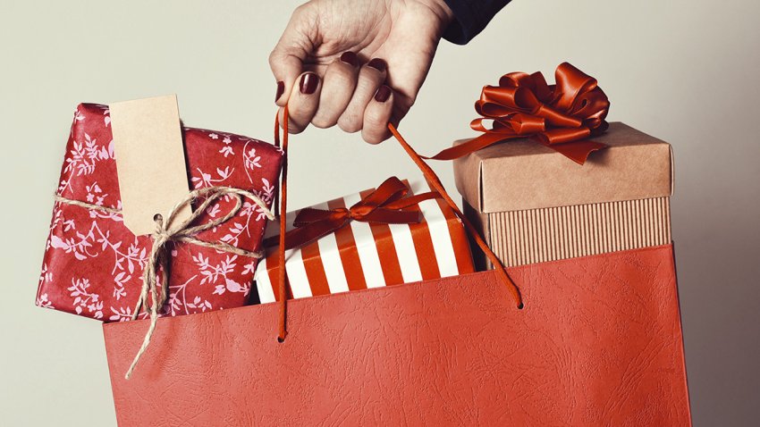 closeup of the hand of a young caucasian woman with her fingernails painted red holding a red shopping bag full of gifts wrapped in different papers