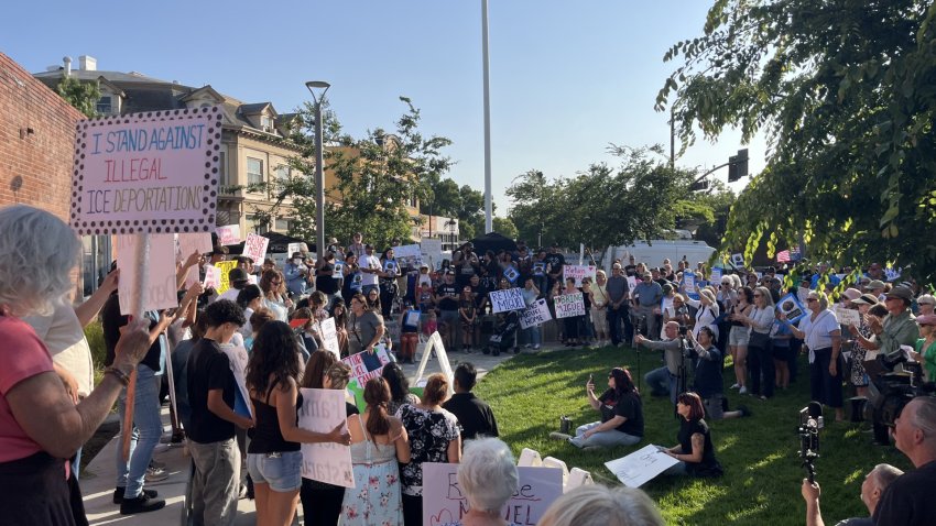 Hundreds of people standing holding signs at an outdoor plaza in downtown Livermore.