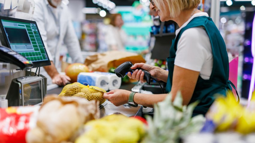 Supermarket cashier scanning groceries at the checkout with barcode reader while customer is waiting, cashier and clients are not recognizable
